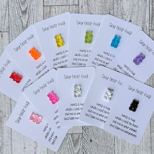 May include: A set of ten cards with gummy bear charms attached. Each card has the text "tiny bear hug" and a short message about the gummy bear. The gummy bears are in various colors, including orange, yellow, pink, red, blue, purple, white, and black.