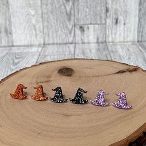 May include: Six pairs of witch hat stud earrings in various colors, including orange, black, and purple. The earrings are displayed on a wooden surface.