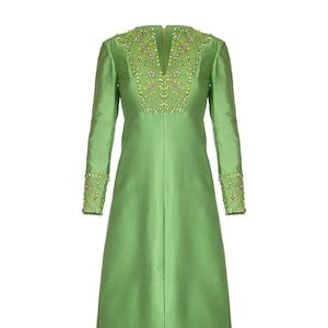 Puede incluir: Un vestido largo de color verde con escote en V y mangas largas. El vestido está adornado con cuentas y lentejuelas verdes, rosas y blancas alrededor del cuello y las mangas.