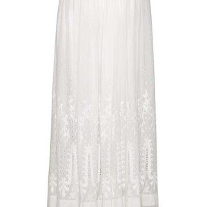 May include: A white maxi skirt with delicate embroidered floral details. The skirt has a flowy silhouette and a tiered ruffle hem.