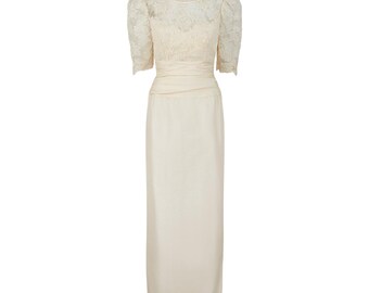 May include: Ivory-colored formal dress. The bodice features a lace overlay with short, puffed sleeves. The waist is cinched with a matching fabric belt, and the skirt is a straight, floor-length design. A classic, elegant style.