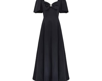 May include: A black maxi dress with a fitted bodice and a full skirt. The dress has short puff sleeves and a large bow at the neckline with a rhinestone embellishment.