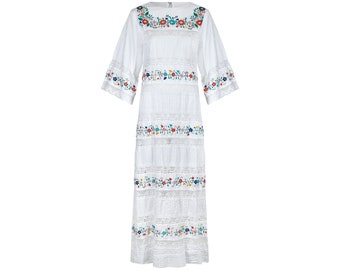 May include: White maxi dress with colorful floral embroidery. The dress has a round neckline and 3/4 sleeves. The embroidery is in a floral pattern and is on the neckline, sleeves, and hem of the dress.