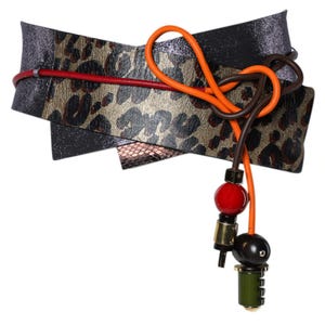 May include: A wide wrap belt featuring a metallic black finish and a central panel with a gold and black leopard print. The belt is accented by a thin red cord and a bright orange cord tied in a knot, ending in dangling red, black, and olive beads.
