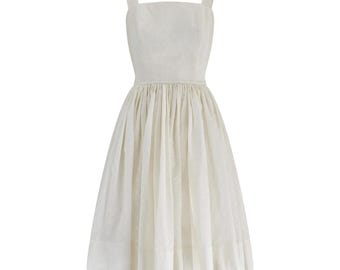 Puede incluir: Vestido color marfil con escote cuadrado y tirantes anchos. El vestido presenta un corpiño ajustado y una falda amplia plisada que llega hasta la pantorrilla. La tela tiene un patrón sutil y texturizado.