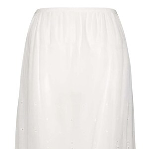 May include: White cotton slip skirt with a delicate eyelet pattern. The skirt is knee-length and has a fitted waistband.