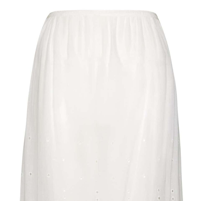May include: White cotton slip skirt with a delicate eyelet pattern. The skirt is knee-length and has a fitted waistband.