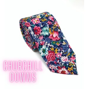 May include: A floral patterned tie with a navy blue background and pink, white, yellow, and green flowers. The tie is rolled up and the text "CHURCHILL DOWNS" is visible in the lower left corner.