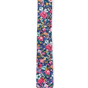 May include: A skinny tie with a floral pattern in shades of pink, blue, green, and yellow. The tie has a white background and features a variety of flowers, including roses and smaller blooms.