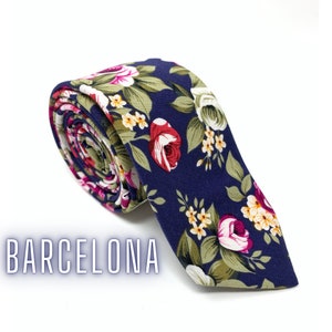 May include: A navy blue tie with a floral pattern featuring pink, white, and green flowers. The tie is rolled up and the text "BARCELONA" is visible in the lower left corner of the image.
