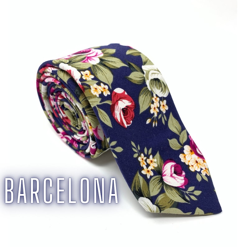 May include: A navy blue tie with a floral pattern featuring pink, white, and green flowers. The tie is rolled up and the text "BARCELONA" is visible in the lower left corner of the image.