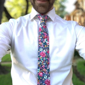 May include: A white dress shirt with a floral patterned tie. The tie has a dark blue background with pink, yellow, and green flowers.