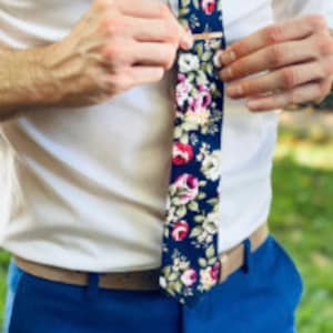 May include: A dark blue tie with a floral pattern featuring pink, red, and white roses. A gold tie clip is attached to the tie.