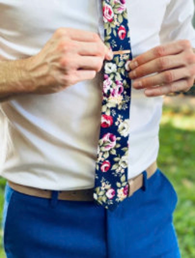 May include: A dark blue tie with a floral pattern featuring pink, red, and white roses. A gold tie clip is attached to the tie.