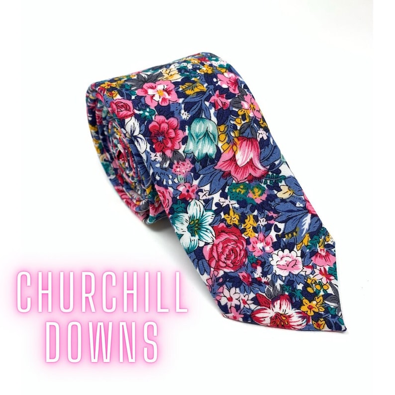 May include: A floral patterned tie with a navy blue background and pink, white, yellow, and green flowers. The tie is rolled up and the text "CHURCHILL DOWNS" is visible in the lower left corner.
