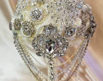 May include: A white bridal bouquet made of silk flowers and rhinestones. The bouquet is adorned with multiple strands of pearls and crystal chains.