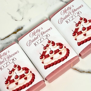 May include: Three pink rectangular bars with white wrappers featuring a cake design with cherries and the text "Molly's Bridal Shower 10.25.26". The cake design includes red cherries and heart-shaped details.