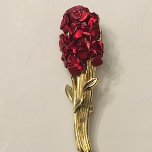 May include: A gold-toned brooch with a bouquet of red flowers. The flowers are made of metal and have a shiny finish.