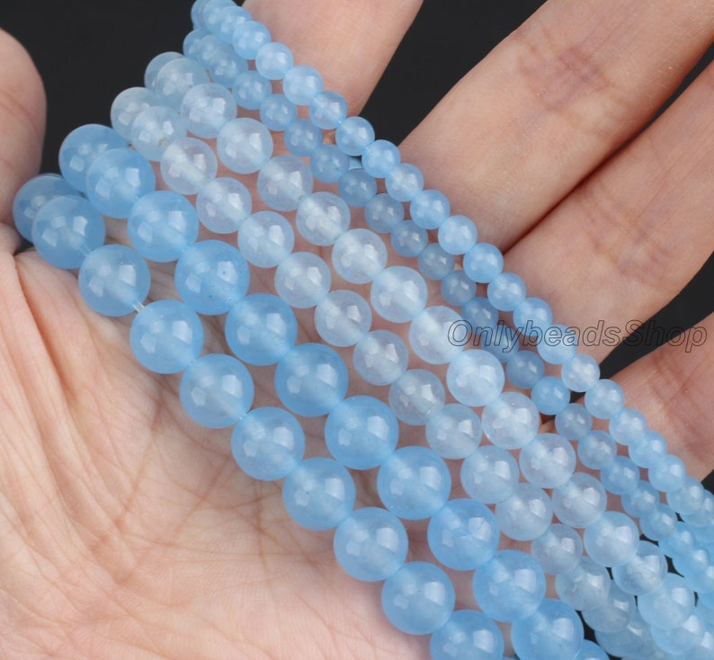 May include: A strand of light blue gemstone beads, with multiple strands of varying sizes, arranged in a graduated pattern. The beads are smooth and round, with a subtle shimmer.
