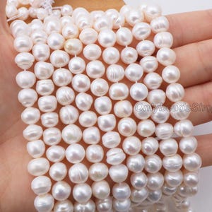 Könnte beinhalten: Nahaufnahme von Strängen weißer, unregelmäßig geformter Perlen. Die Perlen sind aufgereiht und bilden eine dichte, strukturierte Oberfläche. Die Perlen haben eine leuchtende, cremeweiße Farbe und eine glatte, leicht unebene Oberfläche. Das Bild zeigt die natürlichen Variationen jeder Perle.