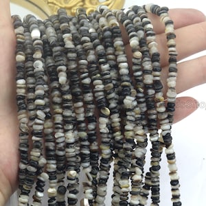 May include: Multiple strands of small, irregular beads in black, grey, and white. The beads, possibly shell or stone, are strung together. The image shows the beads held in a hand. The beads are of varying sizes.