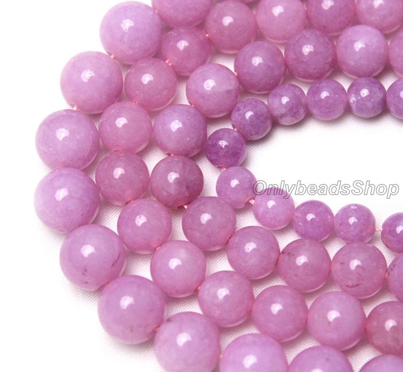 Puede incluir: Una hebra de cuentas redondas de piedras preciosas de color lavanda. Las cuentas son lisas y pulidas, con un ligero brillo. Las cuentas est&aacute;n enhebradas en un hilo transparente.