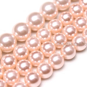 Peut inclure: Un brin de perles de couleur rose pâle. Les perles sont rondes et lisses, avec un léger reflet irisé. Les perles sont disposées en rangée, la rangée du haut chevauchant légèrement la rangée du bas.
