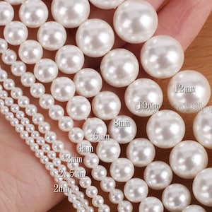 Op de afbeelding: Een assortiment van witte parel kralen in verschillende maten, variërend van 2 mm tot 12 mm. De kralen zijn gerangschikt in rijen, met de grootste kralen bovenaan en de kleinste kralen onderaan.