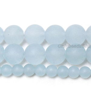May include: A strand of light blue frosted glass beads. The beads are round and smooth, and they are arranged in a row. The beads are of different sizes, with the largest beads in the middle and the smallest beads on the ends.