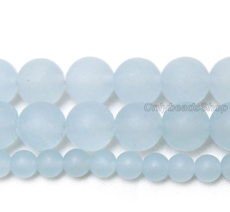 May include: A strand of light blue frosted glass beads. The beads are round and smooth, and they are arranged in a row. The beads are of different sizes, with the largest beads in the middle and the smallest beads on the ends.