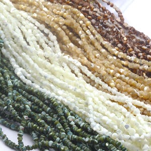 Könnte beinhalten: Nahaufnahme von mehreren Strängen kleiner, unregelmäßig geformter Perlen in verschiedenen Farben. Die Farben umfassen Grüntöne, Weiß, Beige und Braun. Die Perlen sind aufgefädelt und erzeugen einen strukturierten und geschichteten Effekt. Das Bild ist gut beleuchtet.