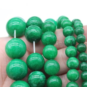 May include: A strand of round, green jade beads. The beads are smooth and polished, with a slight variation in size. The beads are strung on a clear elastic cord.