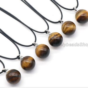 May include: Seven necklaces with black cords and round tiger's eye stone pendants. The pendants are all different sizes and have a golden brown color with a slight shimmer.