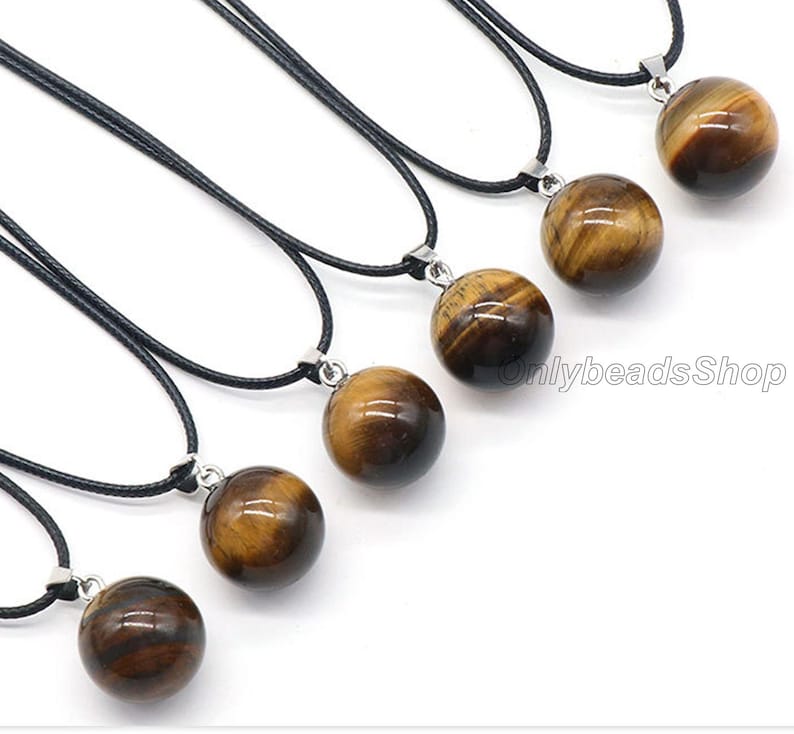 May include: Seven necklaces with black cords and round tiger's eye stone pendants. The pendants are all different sizes and have a golden brown color with a slight shimmer.