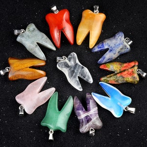 May include: A selection of tooth-shaped pendants in diverse colours and materials, such as red, yellow, and blue. Each pendant features a silver-coloured bail for attaching to a chain. The pendants are displayed on a black surface.