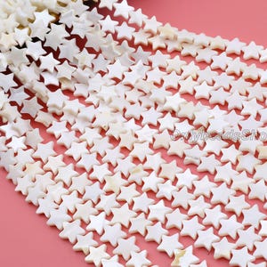 May include: Strands of white star-shaped beads. The beads are made of a pearlescent material and are strung together. The background is a solid pink color. The text "Onlybeads Shop" is visible in the image.