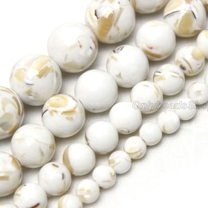 May include: A strand of white and cream-colored round shell beads. The beads are arranged in a graduated size, with the largest beads at the top and the smallest beads at the bottom. The beads have a natural, organic look and feel.