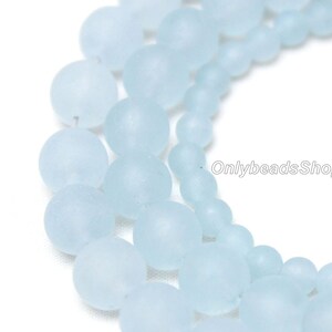 May include: A strand of light blue frosted glass beads. The beads are round and have a smooth, matte finish.