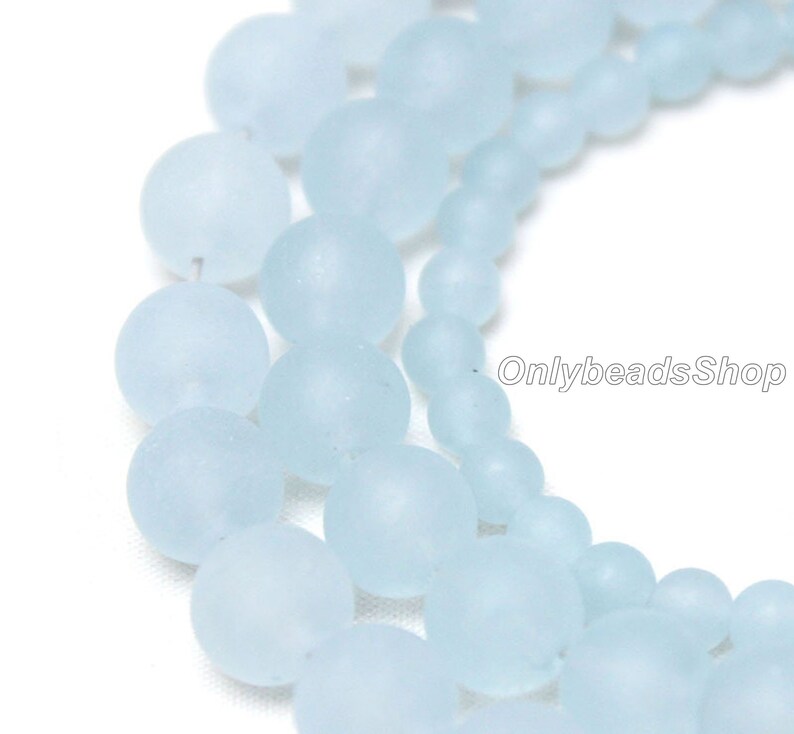 May include: A strand of light blue frosted glass beads. The beads are round and have a smooth, matte finish.