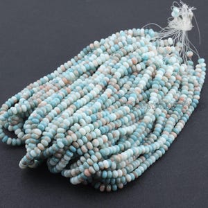 Pu&ograve; includere: Fili di piccole perline rotonde nei toni del blu, pesca e bianco. Le perline sono infilate insieme, creando un'esposizione strutturata e colorata. Le perline sono probabilmente destinate alla creazione di gioielli.