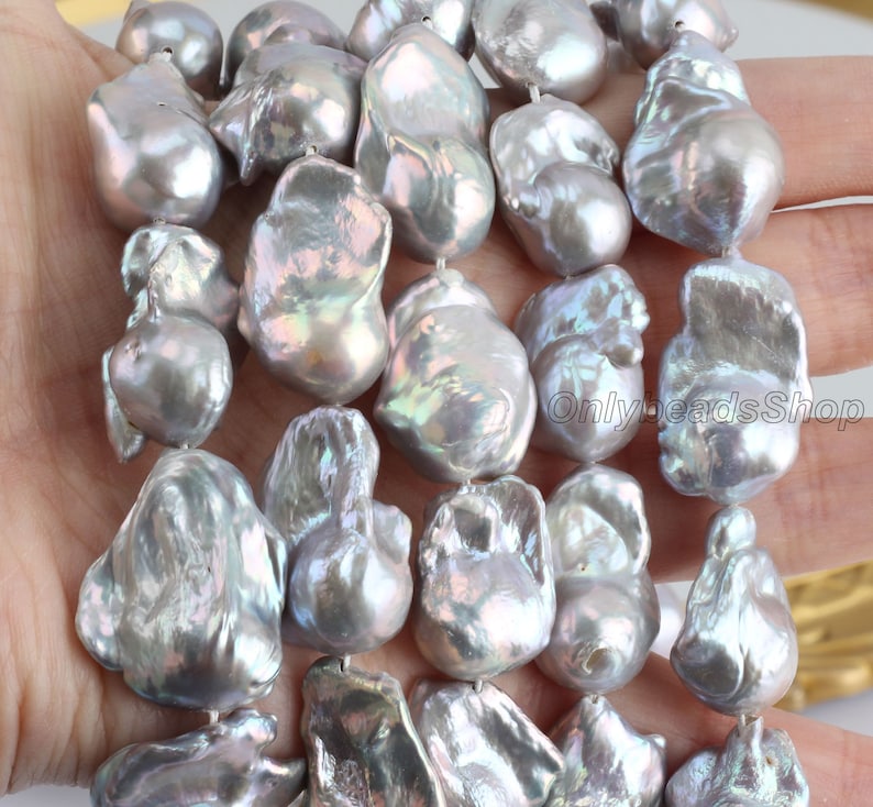 May include: A strand of large, irregular, baroque pearls. The pearls are a silvery grey colour with iridescent highlights.