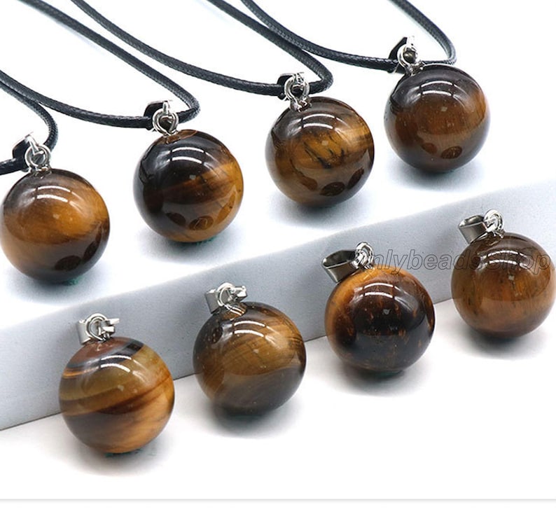 May include: Eight gold and brown tiger's eye stone ball pendants on black cords. Each pendant is approximately 1 inch in diameter.