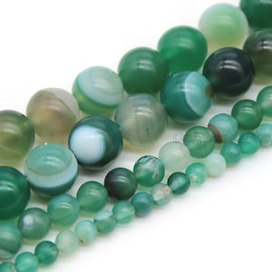 May include: A strand of green agate beads with white and green patterns. The beads are round and smooth, and they are strung on a clear thread. The beads are of varying sizes, with some being larger than others.