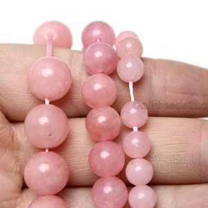 May include: A strand of pink rose quartz beads, with a variety of sizes, strung on a white cord. The beads are smooth and polished, with a subtle shimmer.