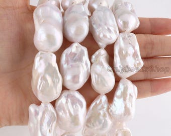 May include: A strand of large, irregular, white baroque pearls with a high-lustre, iridescent finish. The pearls are strung together, displaying varied, organic shapes and smooth, reflective surfaces. The text OnlybeadsShop is visible.