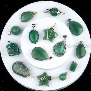 Puede incluir: Una colección de 13 colgantes de aventurina verde en varias formas y tamaños, incluyendo estrellas, lágrimas, óvalos y rectángulos. Algunos colgantes están envueltos en alambre dorado. Los colgantes se muestran en una superficie circular blanca.