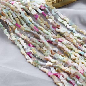 Può includere: Fili di perline di conchiglia colorate nelle tonalità del bianco, rosa, giallo e verde. Le perline hanno una forma a mezzaluna e sono infilate insieme. Le perline sono disposte in diagonale.