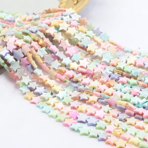 May include: A collection of pastel-coloured star-shaped beads in shades of pink, yellow, green, and blue. The beads are strung together, creating a flowing pattern. The image includes the text "OnlybeadsShop".