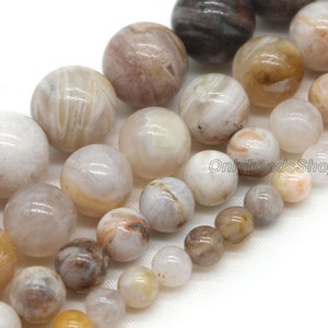 May include: A collection of white, brown, and beige agate beads with a variety of patterns. The beads are round and smooth, and they are arranged in a line.