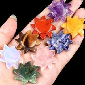 Może przedstawiać: Kolekcja rzeźb z kamieni szlachetnych w kształcie słońca w różnych kolorach, w tym fioletowym, czerwonym, żółtym, niebieskim, brązowym, różowym, zielonym i opalizującej bieli. Każde słońce ma szczegółowy, rzeźbiony wzór. Kamienie szlachetne są trzymane w dłoni na czarnym tle.